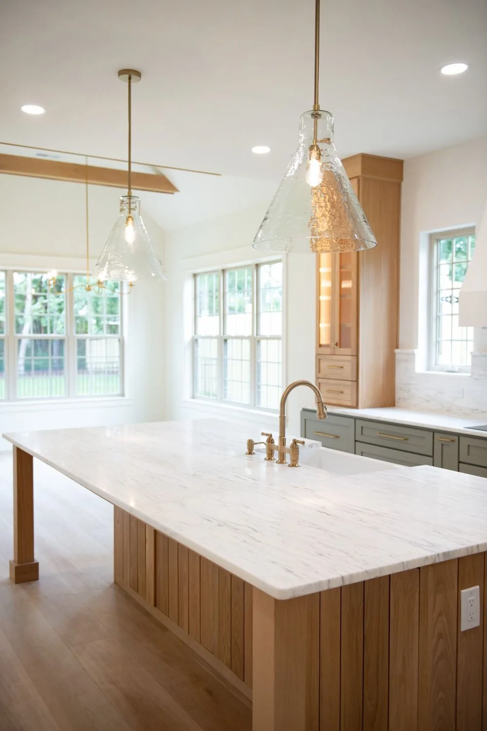 Kitchen with a marble island, exposed beams and brass fixtures built by Delaney's Coastal Construction
