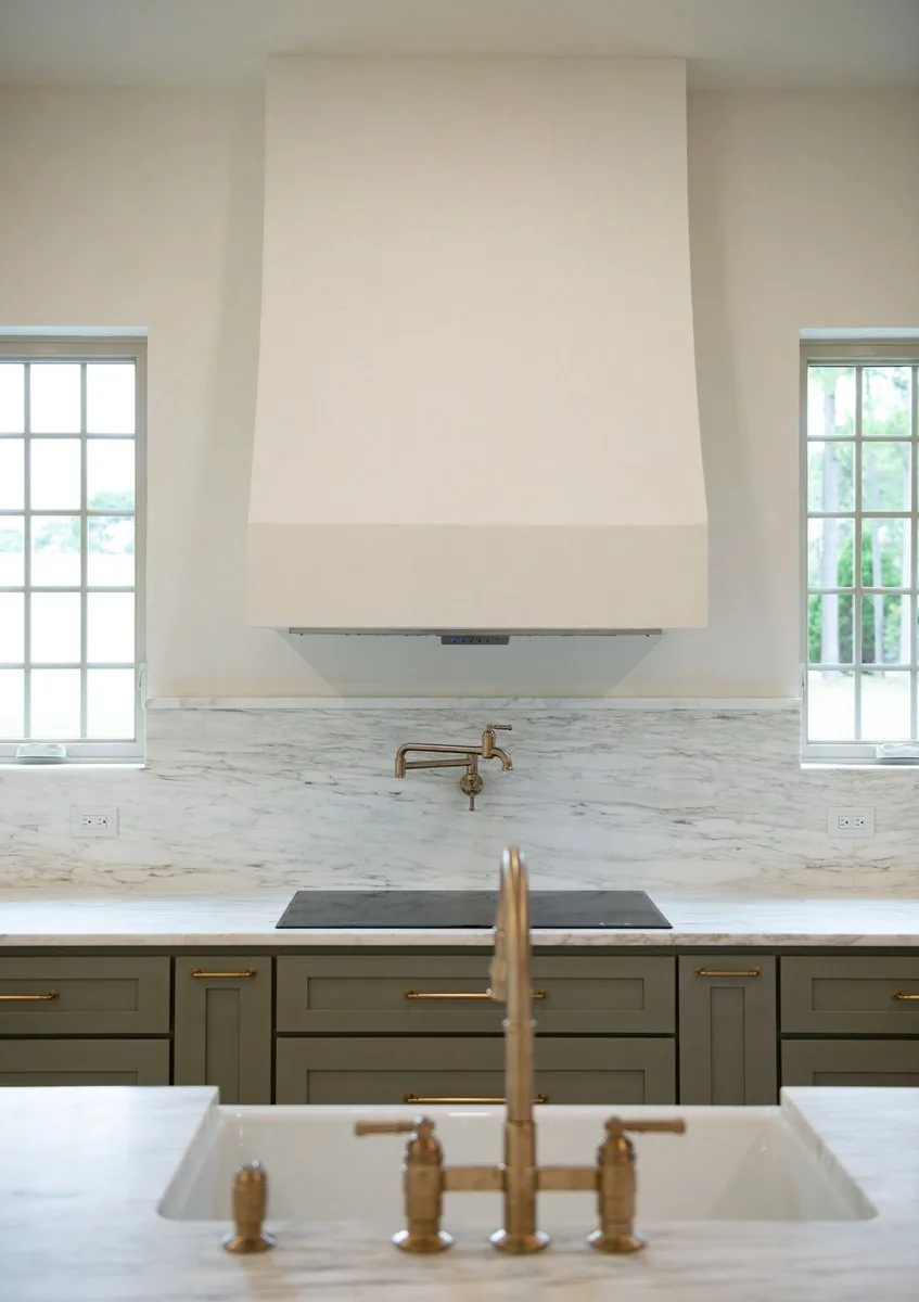 Remodeled kitchen with a plaster range hood, brass faucet and stone counters