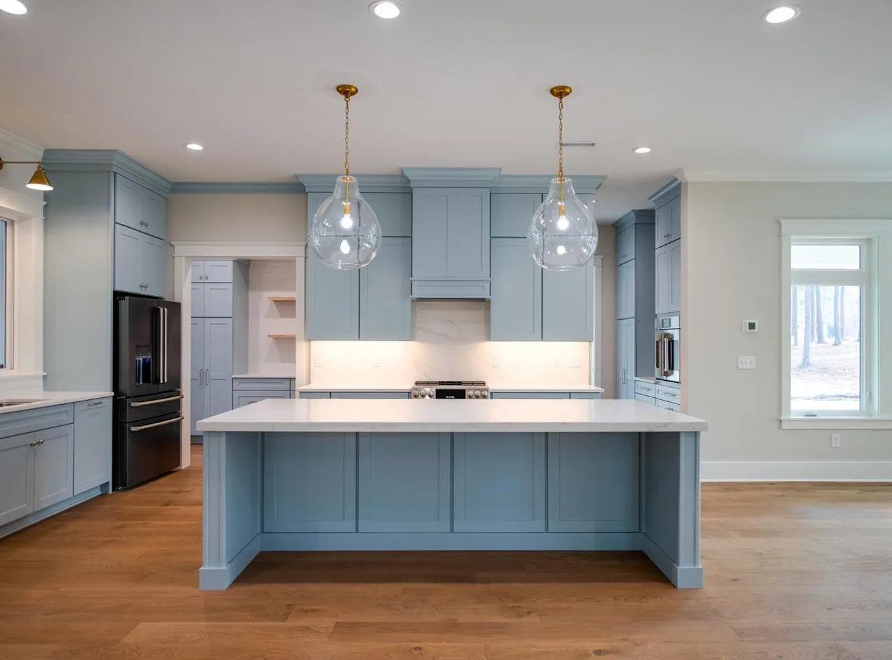 Kitchen with pale blue cabinets, glass pendants and a large island