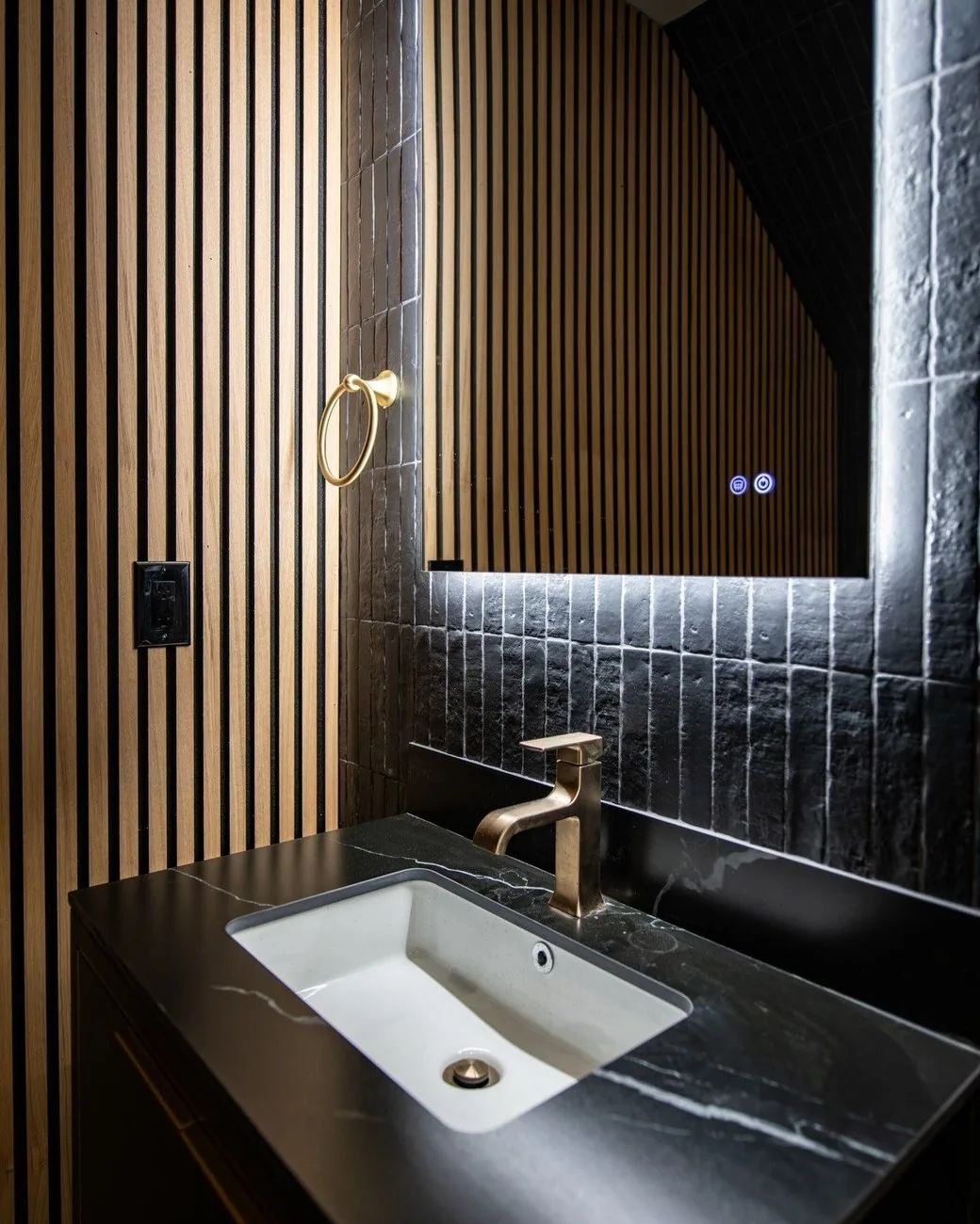 Powder room with a slatted wood wall, backlit mirror and stone vanity